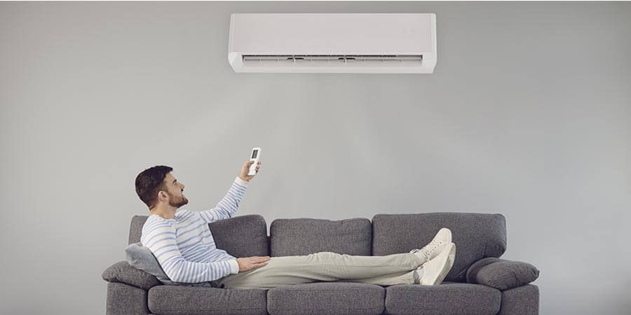 Man sitting on the couch turning on ductless AC unit