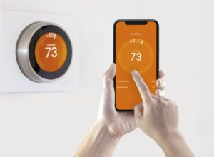 Orange Smart Thermostat Behind Phone Using Thermostat App