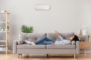 Woman Laying On Couch Adjusting Temperature On Ductless Hvac System